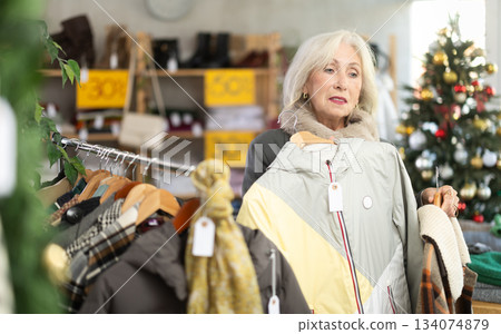 mature woman choosing coats and jackets in a Christmas shop mature woman choosing coats and jackets in a Christmas shop 134074879