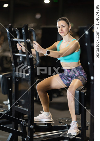 Woman training hips on standing abductor machine at gym 134074898
