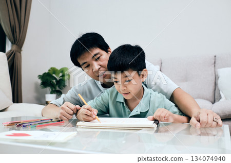 Asian father helps his son draw at home, sharing a caring and creative family moment indoors 134074940