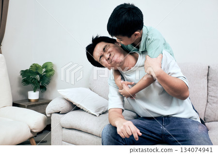 Asian father and son share playful moment on the couch as the boy hugs and kisses his dad lovingly 134074941