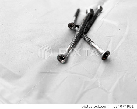 Collection of metal screws scattered on light surface. Shiny metal, details of spiral threads and flat heads. Simplicity of tools, ideal for construction, woodworking or DIY projects, functional 134074991