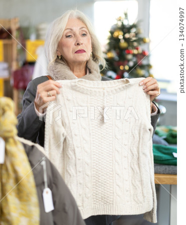 Uncertain mature woman choosing sweater in clothing store 134074997