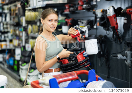 Woman chooses and buys paint spray gun in hardware store Woman chooses and buys paint spray gun in hardware store 134075039