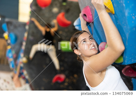 Confident young woman scaling artificial climbing wall in climbing gym 134075069