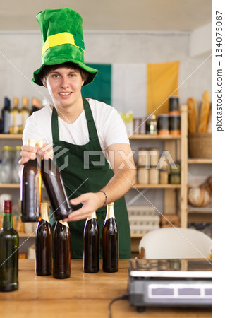 Smiling man seller in traditional Irish green cap offers Irish ale on St. Patrick Day in supermarket Smiling man seller in traditional Irish green cap offers Irish ale on St. Patrick Day in supermarket 134075087