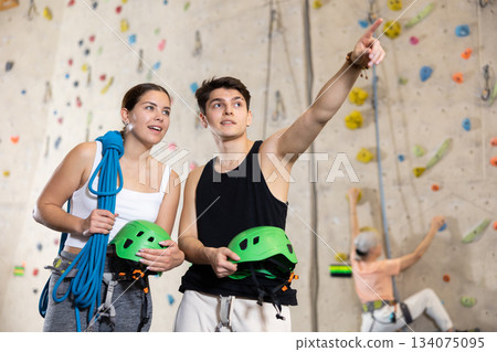 Motivated sporty young people, man and woman standing with special equipment before climbing up bouldering wall in amusement center 134075095