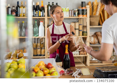 Friendly female salesperson offers to buy bottle of wine to male customer at grocery store 134075100