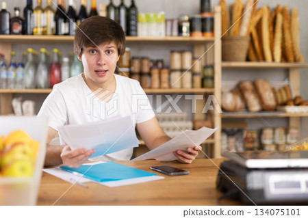 Young manager of a grocery supermarket keeps count of goods and makes entries in journal 134075101