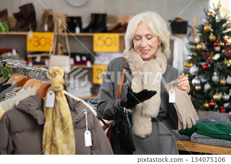 mature woman chooses gloves against the background of a Christmas tree 134075106