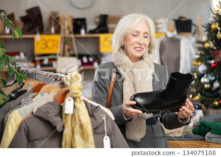 Positive old lady choosing platform boots in clothing store 134075108