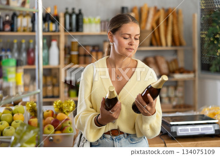 Girl buyer examines beer bottles, chooses right manufacturer, takes various bottles from shelf. Girl buyer examines beer bottles, chooses right manufacturer, takes various bottles from shelf. 134075109