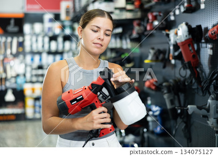 Beautiful girl planning home renovation and choosing paint sprayer in hardware store 134075127