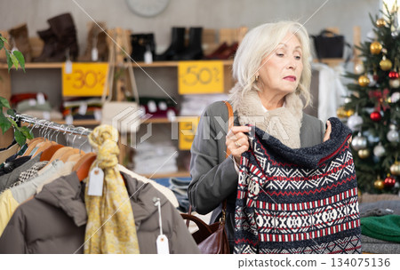Uncertain mature woman choosing sweater in clothing store Uncertain mature woman choosing sweater in clothing store 134075136