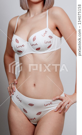 Woman in a white floral lace lingerie set posing with one foot slightly raised Woman in a white floral lace lingerie set posing with one foot slightly raised 134075158