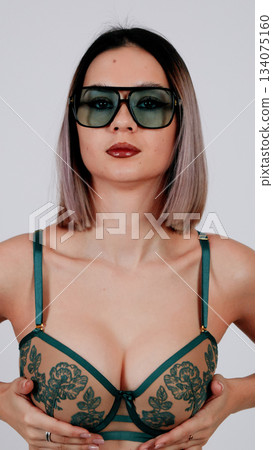 Woman in a dark green lingerie set with sunglasses posing provocatively Woman in a dark green lingerie set with sunglasses posing provocatively 134075160