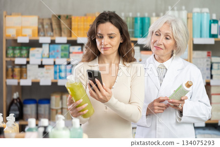 Woman in pharmacy scans QR code on shampoo, senior woman pharmacist in background Woman in pharmacy scans QR code on shampoo, senior woman pharmacist in background 134075293