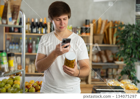 Young man scans a jar of olives on his phone Young man scans a jar of olives on his phone 134075297