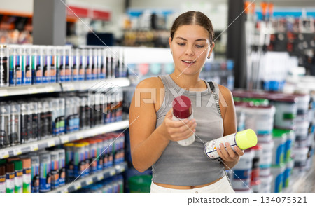 Girl young woman chooses picks up buys aerosol paint varnish solvent in construction store Girl young woman chooses picks up buys aerosol paint varnish solvent in construction store 134075321