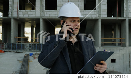 Construction talking on a smartphone while overlooking the busy work site Construction talking on a smartphone while overlooking the busy work site 134075324