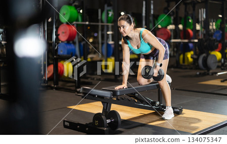 Woman trains muscles of arms, perform exercises with dumbbell Woman trains muscles of arms, perform exercises with dumbbell 134075347