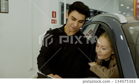 Smiling couple embracing in the driver's seat of their new car in the showroom Smiling couple embracing in the driver's seat of their new car in the showroom 134075383