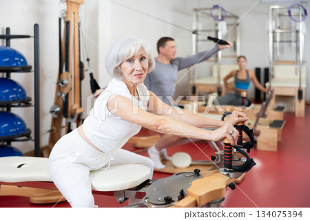 Mature woman during Pilates training performs exercises and tasks on heron pulley tower Mature woman during Pilates training performs exercises and tasks on heron pulley tower 134075394