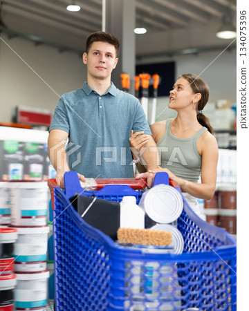 Spouses shopper stand with trolley filled with paint goods for repair and coloring in store sales hall. 134075396