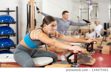 Young girl during Pilates training performs exercises and tasks on heron pulley tower Young girl during Pilates training performs exercises and tasks on heron pulley tower 134075401
