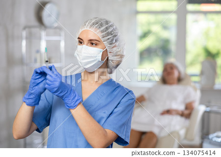 Portrait of young female doctor in scrub and mask holding syringe. Portrait of young female doctor in scrub and mask holding syringe. 134075414