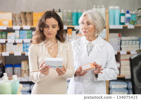 European woman chooses a package of pills in a pharmacy with a pharmacist 134075415