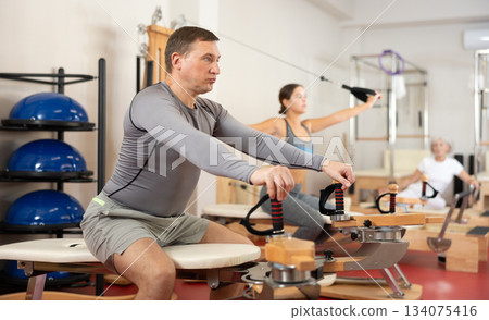 Adult man stretching her arms using pilates machine Adult man stretching her arms using pilates machine 134075416