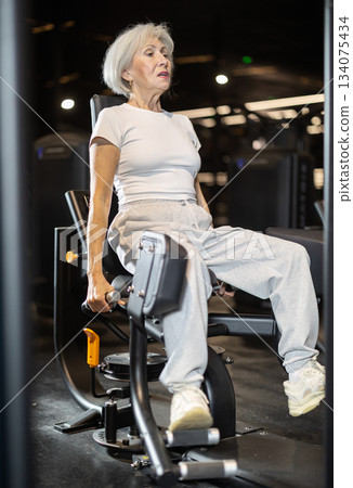Older woman training on hip abduction machine at gym 134075434