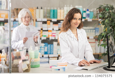 Female pharmacist using computer, companion at background Female pharmacist using computer, companion at background 134075575