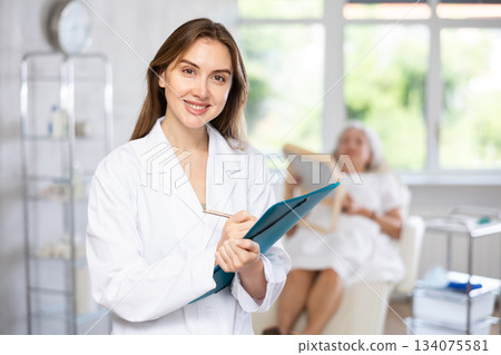 Female doctor in scrub holding clipboard. Female doctor in scrub holding clipboard. 134075581