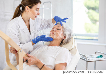 Mature patient with mirror, doctor with gloves Mature patient with mirror, doctor with gloves 134075582