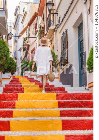 Young woman in a white dress walking up the colourful Spanish Steps in the Arrabal old town district of Calpe, Spain 134076815