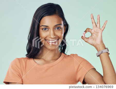 Portrait, perfect hand gesture and woman in a studio with a positive, confident and happy mindset. Happiness, smile and young Indian female model with a ok sign language isolated by green background. 134076969