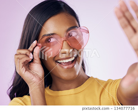 Heart, glasses and selfie by indian woman in studio happy, cheerful and fun on purple background. Sunglasses, pose and female gen z fashion influencer smile for profile picture, photo or blog post 134077716