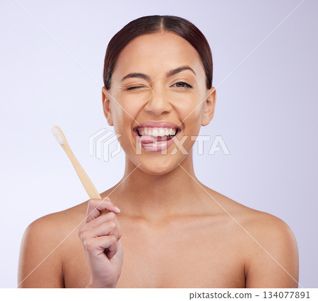 Portrait, wink or happy girl brushing teeth with smile for healthy oral or dental hygiene in studio. Face, beauty or Brazilian woman model cleaning mouth with a natural bamboo wooden toothbrush 134077891
