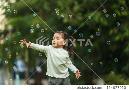 happy toddler girl running and playing soap bubble in park 134077950