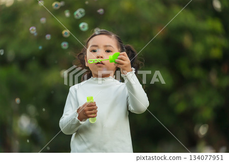 happy toddler girl blowing soap bubbles in park 134077951