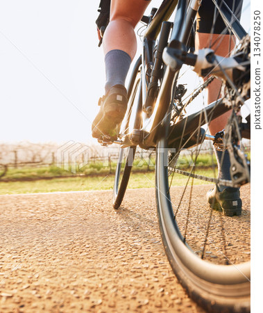 Bicycle closeup, countryside ride and person on a bike with speed for sports race on a gravel road. Fitness, exercise and athlete legs doing sport training in nature on a trail for cardio and workout 134078250