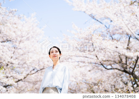 Young woman looking up at cherry blossoms Lifestyle image 134078408
