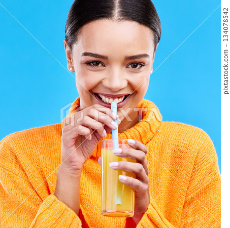 Happy woman, portrait and straw for drinking orange juice in studio, blue background and smile. Female model, glass and sip of fruit cocktail for nutrition, vitamin c diet and detox vegan smoothie 134078542