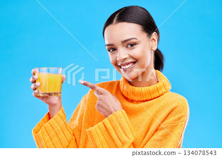 Happy woman, portrait and pointing to orange juice in studio, blue background and backdrop. Female model, drinking glass and fruit cocktail beverage for nutrition, diet and detox health of vitamin c 134078543