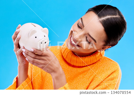 Happy woman, money and piggy bank for investment, budget or finance against a blue studio background. Female smile holding savings of cash or coin for change, profit or investing in financial freedom Happy woman, money and piggy bank for investment, budget or finance against a blue studio background. Female smile holding savings of cash or coin for change, profit or investing in financial freedom 134078554