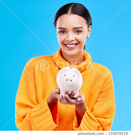 Happy woman, money and piggy bank for investment, budget or finance against a blue studio background. Portrait of female smile holding savings, cash or coin for profit, investing or financial freedom Happy woman, money and piggy bank for investment, budget or finance against a blue studio background. Portrait of female smile holding savings, cash or coin for profit, investing or financial freedom 134078559