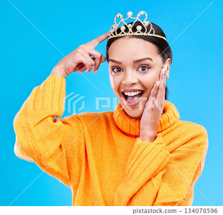 Pointing, crown and portrait of woman in studio for celebration, princess or wow party. Smile, beauty or fashion with female tiara on blue background excited for achievement, winner and prom surprise 134078596