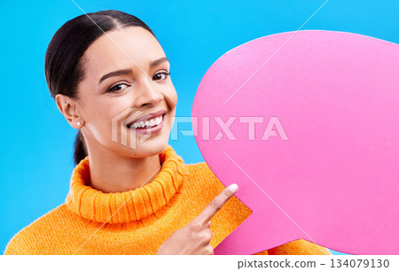 Speech bubble, smile and portrait of woman pointing to banner in studio for advertising on blue background. Face, happy and girl with poster, mockup and space for social media, announcement or news 134079130