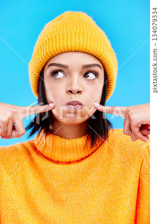 Silly, goofy and young woman in a studio with a comic, funny and crazy face expression. Funny, humor and beautiful female model from Puerto Rico touching her cheeks isolated by a blue background. 134079334